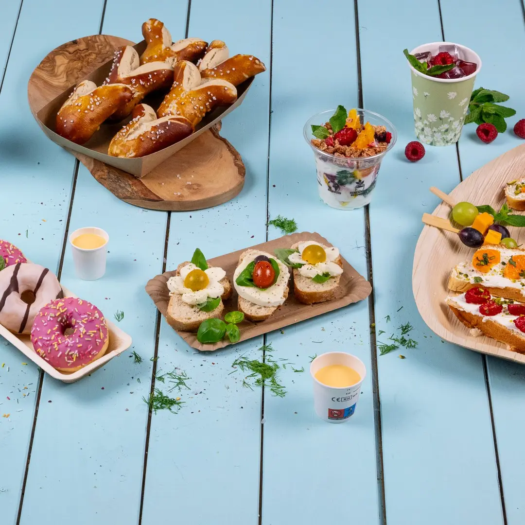 Een verscheidenheid aan fingerfood, waaronder pretzels, sandwiches met toppings, donuts en fruitbekers op een blauwe houten tafel.