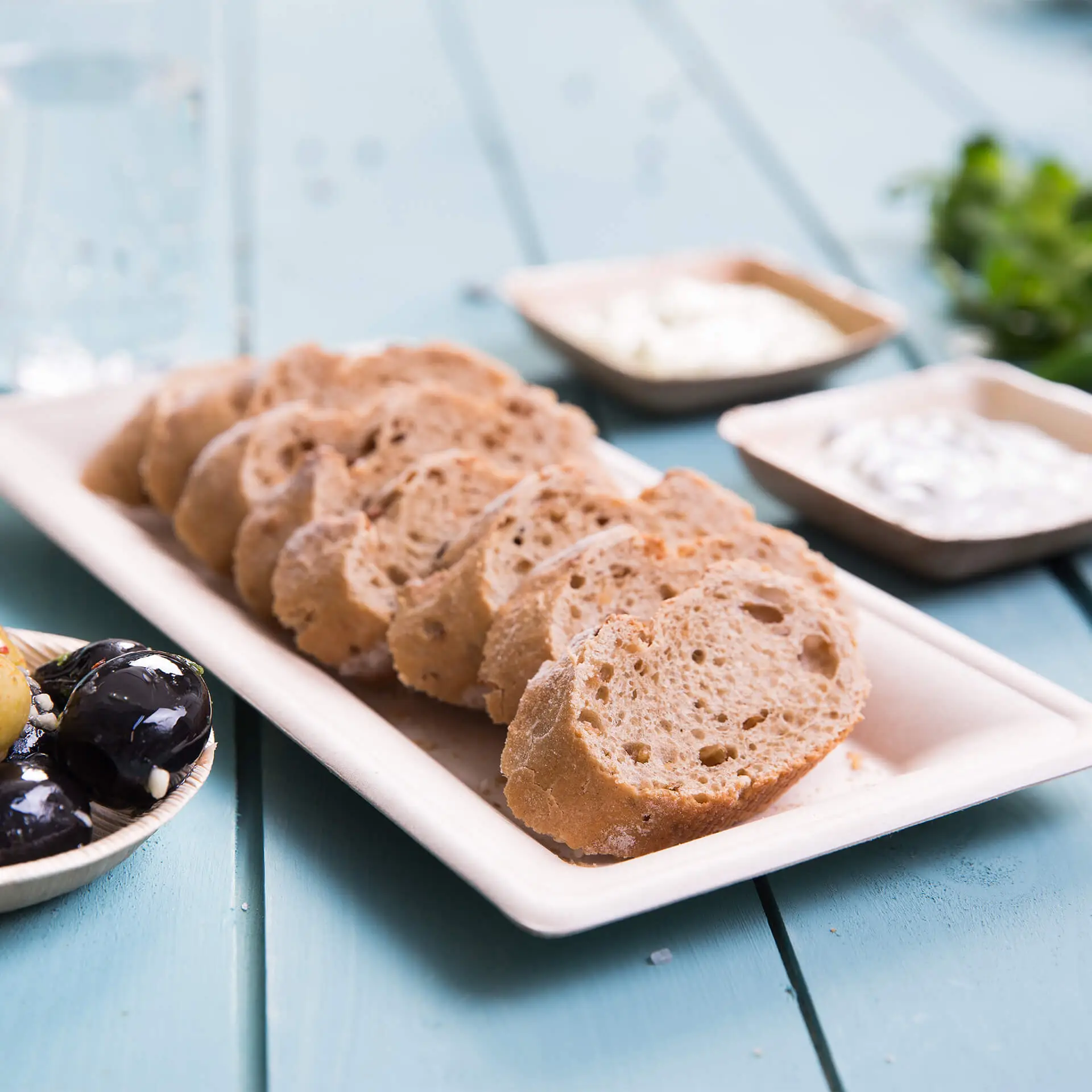 Gesneden brood geserveerd op een rechthoekig suikerriet bord, met dips in kleine kommetjes erbij.