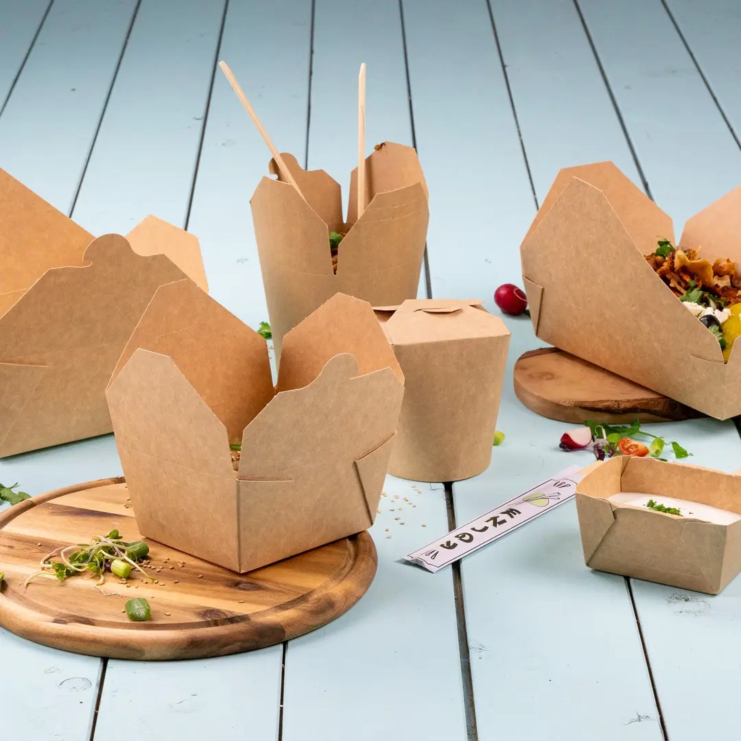 Bruine kartonnen voedselcontainers in verschillende vormen op een houten plank met verse ingrediënten eromheen.