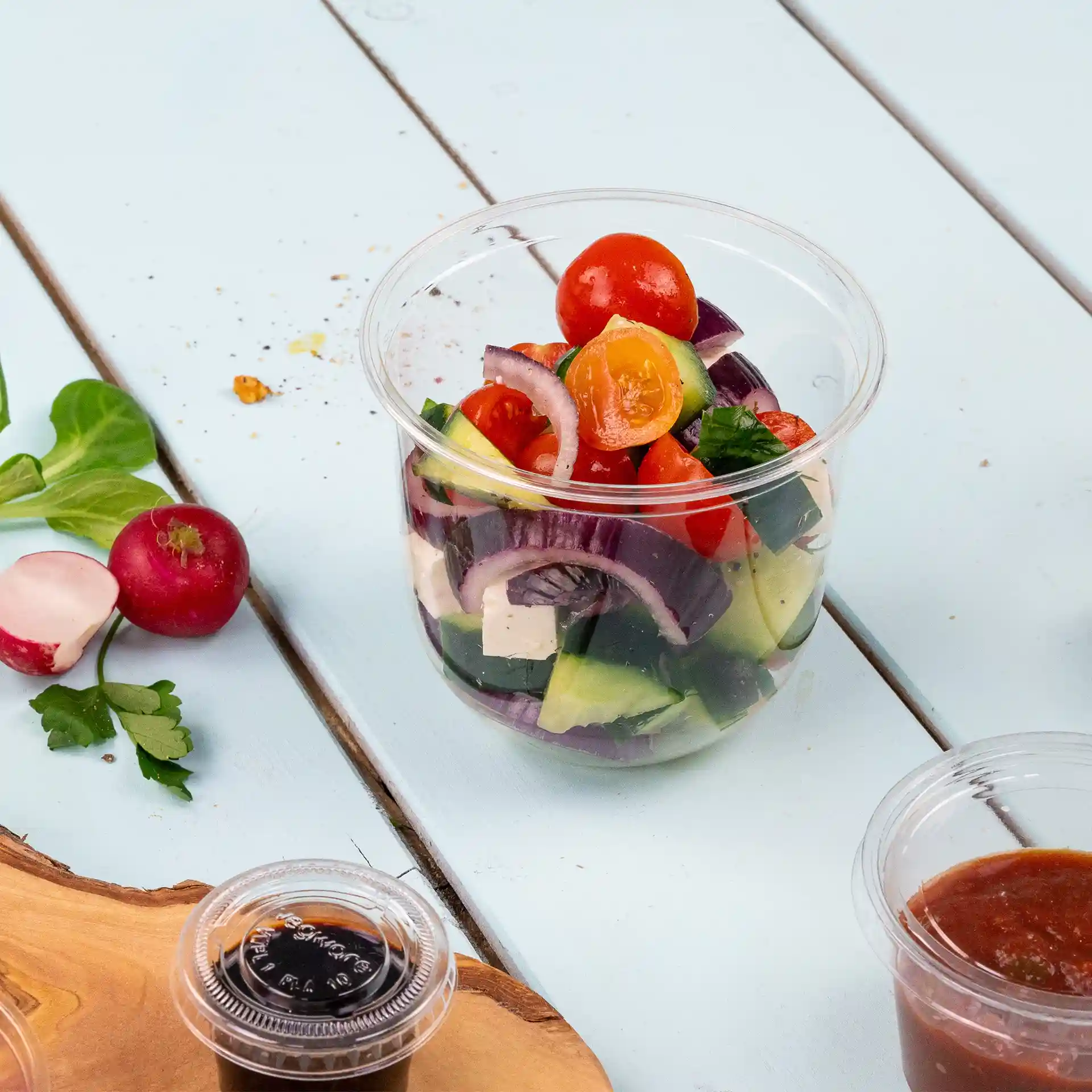 Transparante beker gevuld met gemengde salade-ingrediënten, waaronder cherrytomaten, komkommer en rode ui.