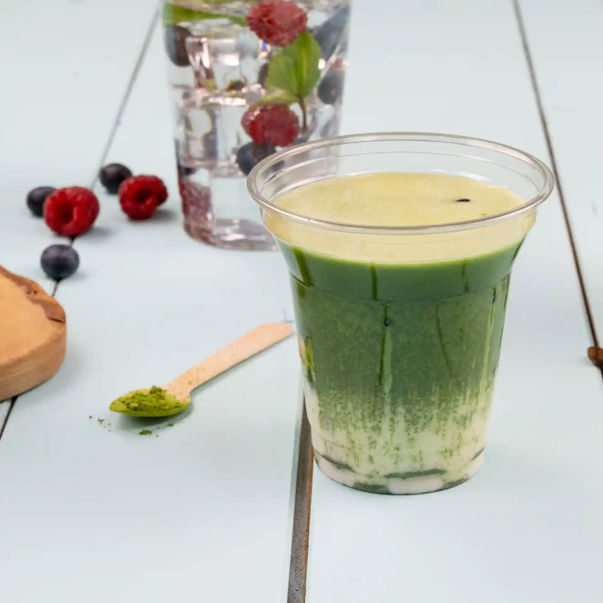 Duidelijke rPET-beker gevuld met groene drank, met een houten lepel en bessen op de achtergrond.