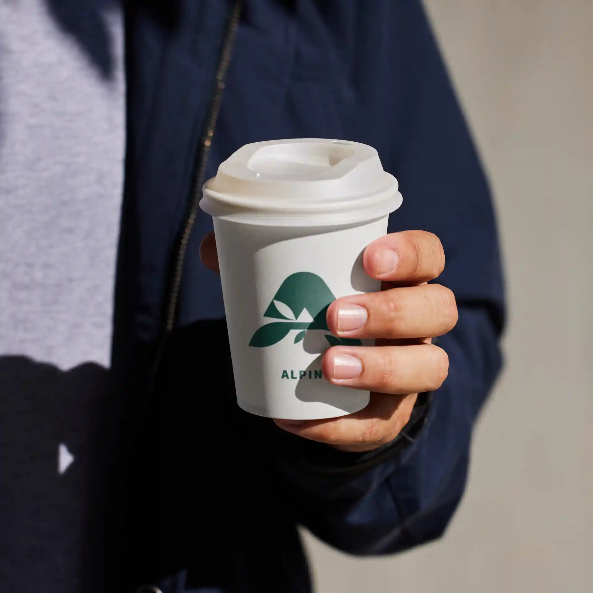 Witte beker met logo, vastgehouden in een hand, met een deksel en een ronde vorm.