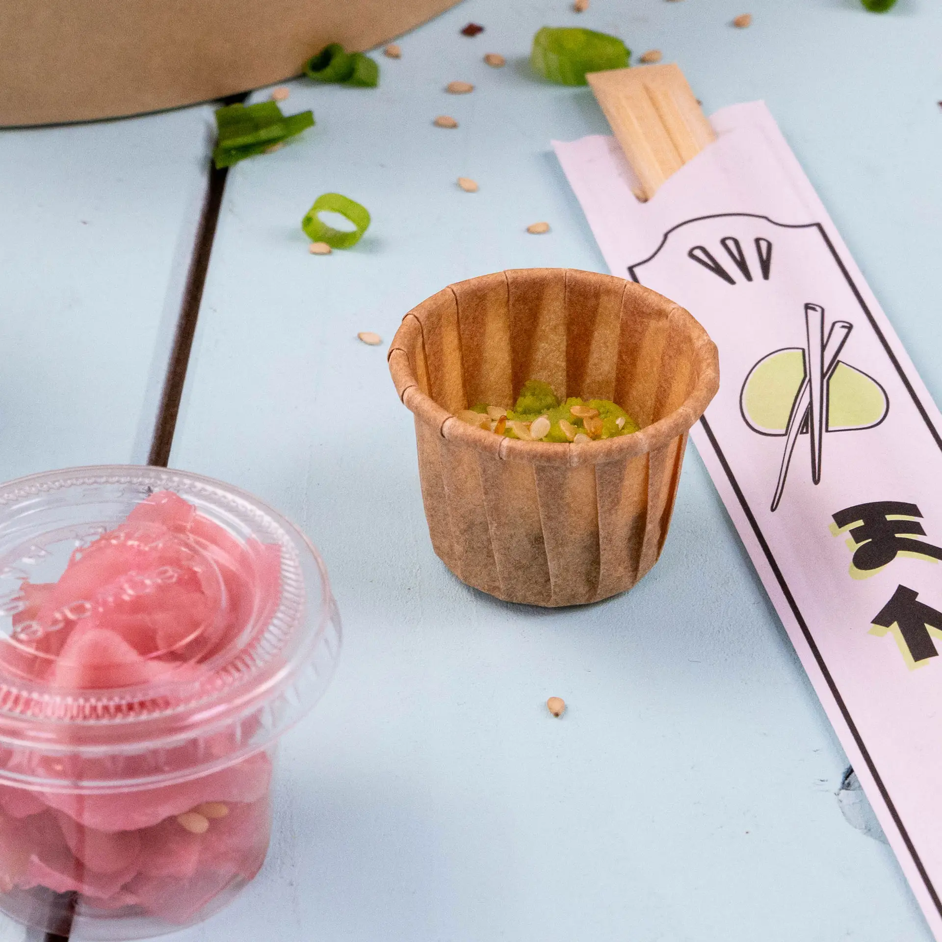 Bruine papieren beker voor dips en sauzen, 15 ml capaciteit, met sesamzaadjes en gehakte lente-uien naast ingemaakte gember en eetstokjes.