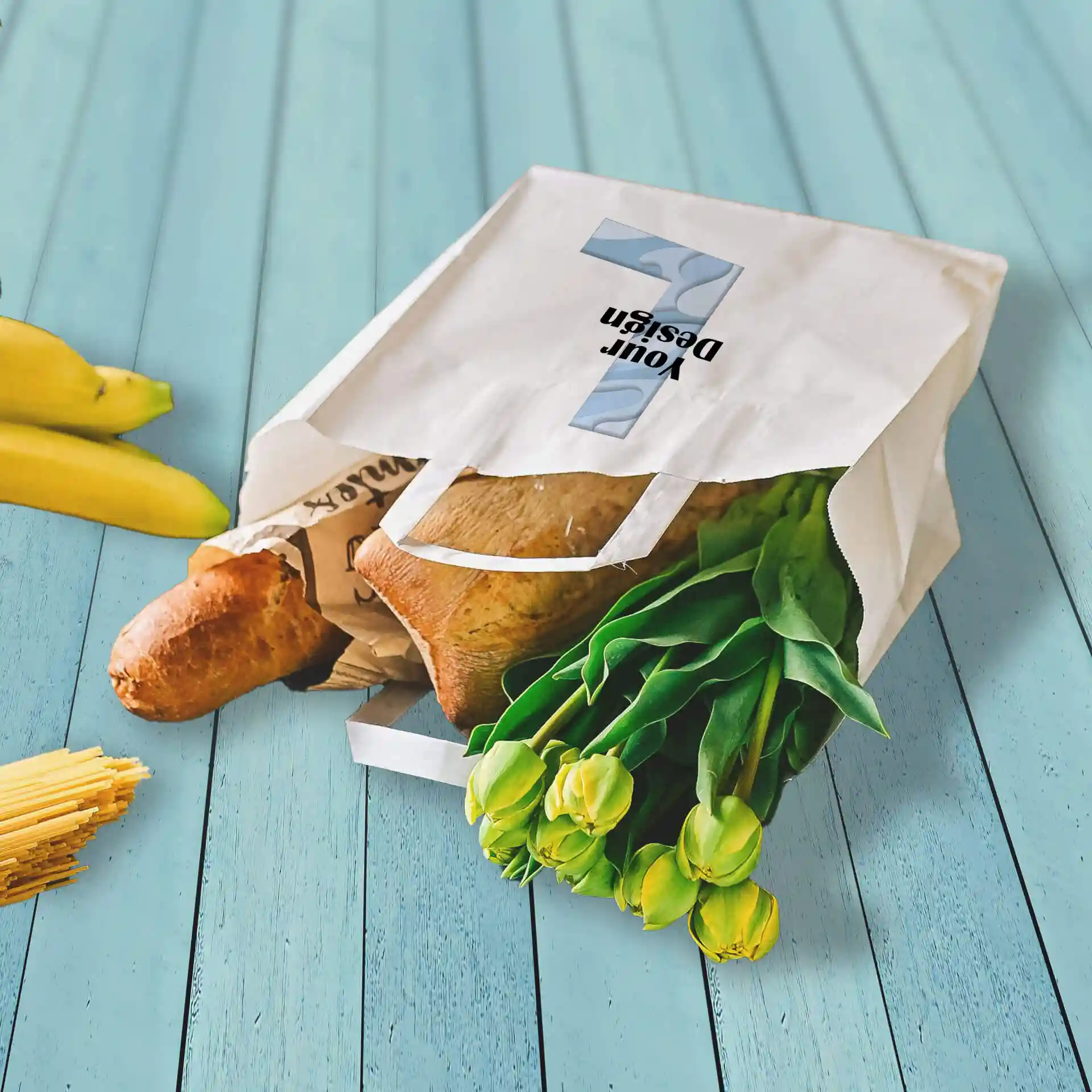Witte papieren tas met boodschappen, waaronder een baguette en tulpen, op een blauwe houten ondergrond.