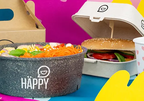 Stapel kleurrijke bakjes met het label "HAPPY BOWL" in verschillende ontwerpen, met daarachter een aparte voedselcontainer.