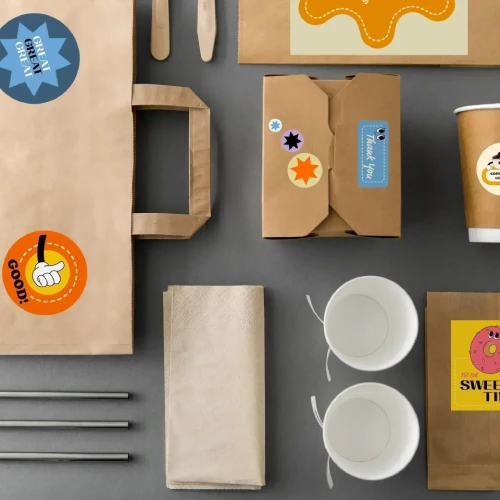 Een collectie wegwerp voedselverpakking, inclusief een papieren tas, dozen, bekers en bestek met kleurrijke labels en stickers.