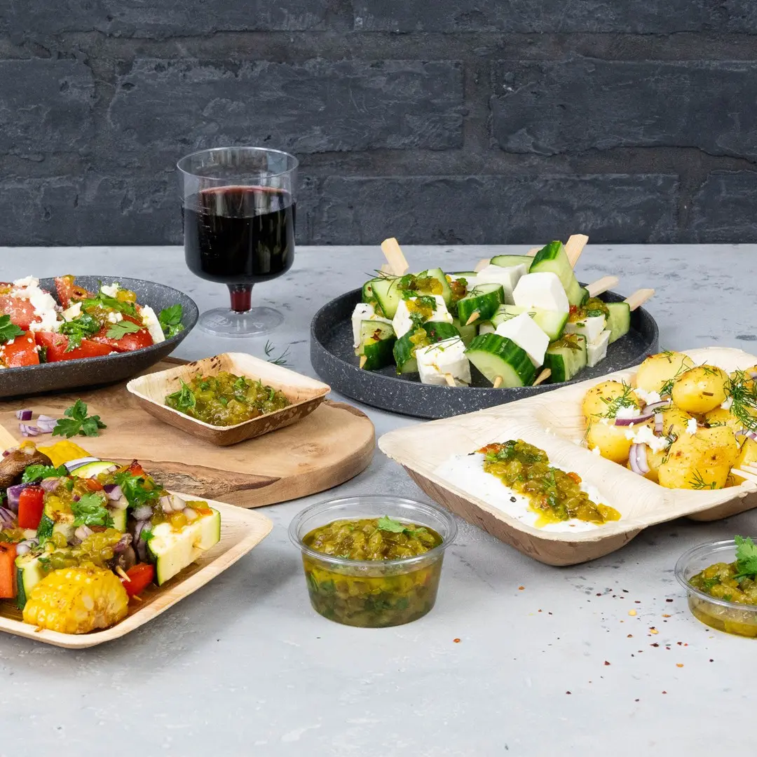 Een verscheidenheid aan fingerfood, waaronder salades, komkommer- en kaasprikkers en sauzen, met een glas rode wijn op de achtergrond.
