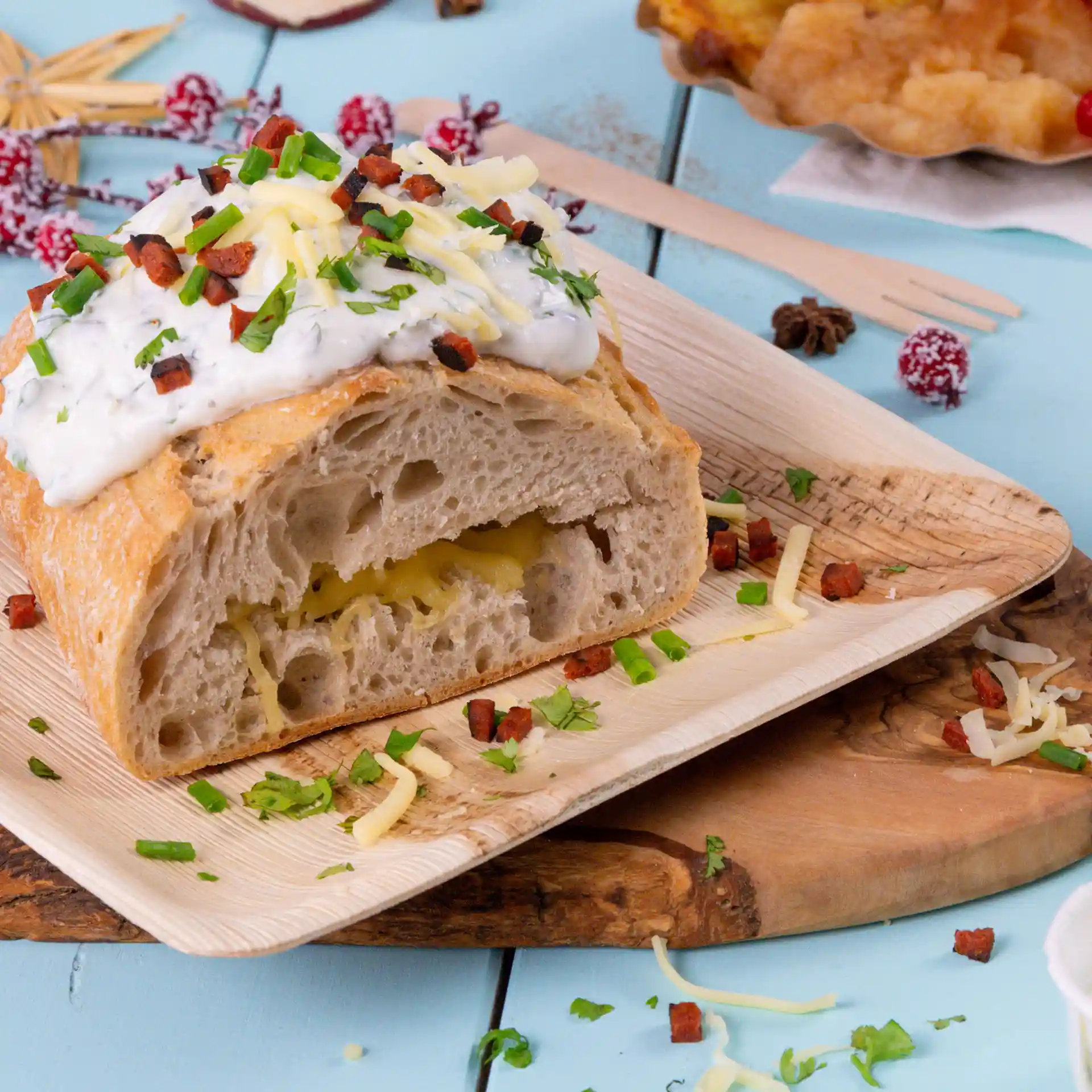 Vierkante palmbladplaat met een gesneden brood, belegd met saus, kaas en kruiden, op een houten oppervlak.