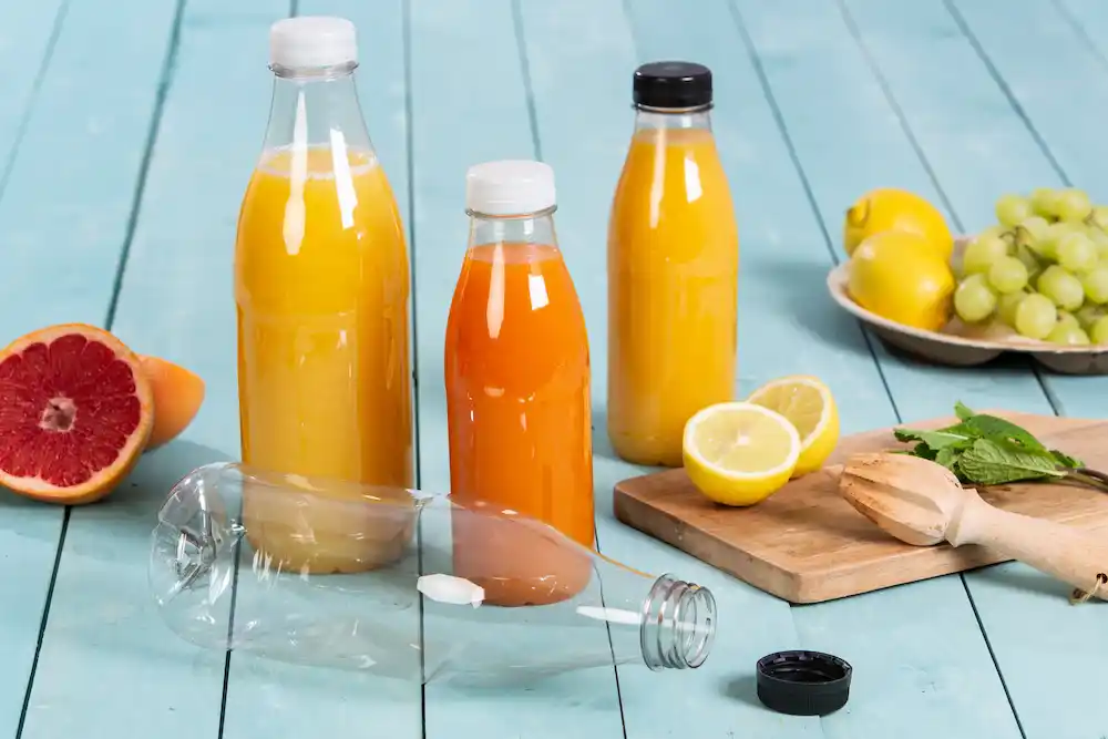 Twee glazen flessen gevuld met sinaasappelsap en gele sap, een gesneden citroen, druiven en een halve grapefruit op een houten oppervlak.