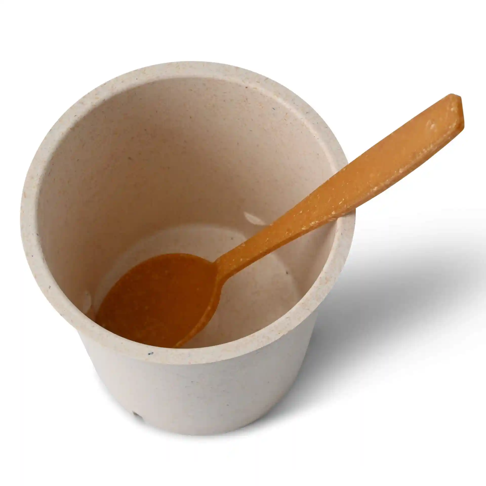 Ronde crème-witte herbruikbare beker met een bijpassende oranje lepel erin, van bovenaf gezien.
