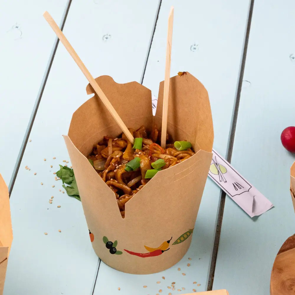 Container met noedels, belegd met lente-uitjes en sesamzaadjes, vergezeld van houten chopsticks.