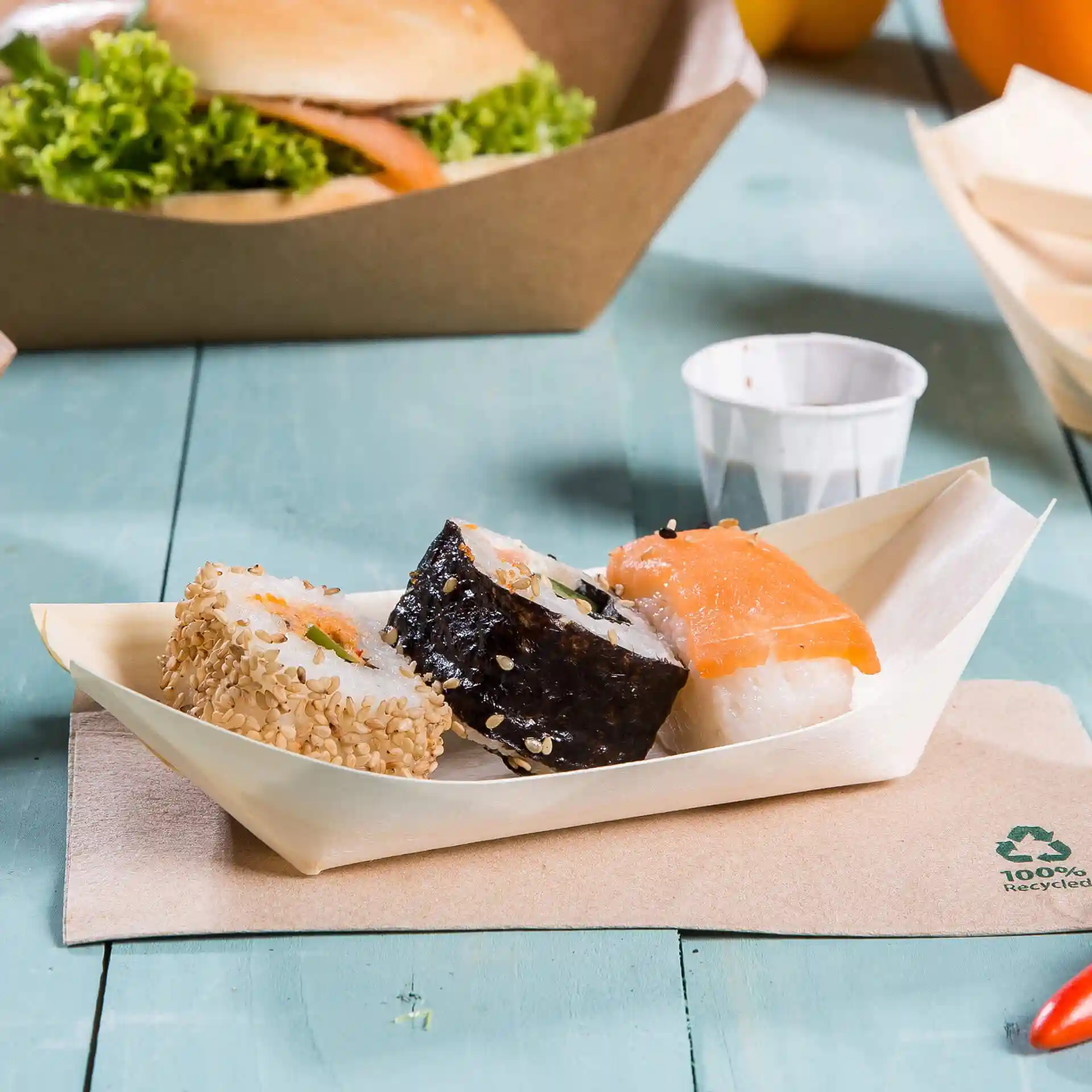 Drie stukken sushi geserveerd in een houten bootvormige schaal op een lichtblauwe ondergrond.