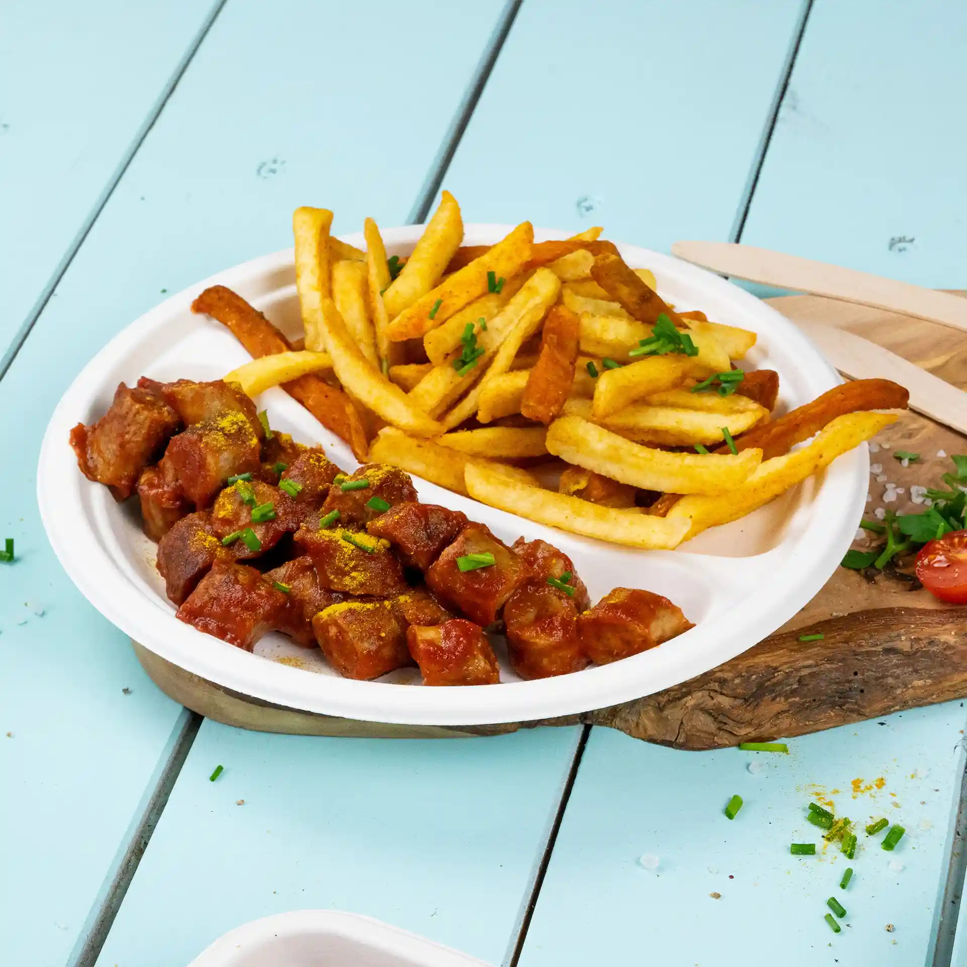 Ronde witte suikerrietplaat met twee compartimenten, één gevuld met in blokjes gesneden vlees in saus en de ander met frietjes.