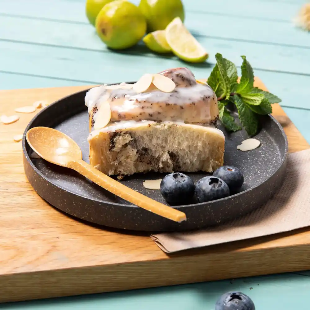 Dessertsneetje op een donker bord met blauwe bessen, amandelschaafsel, een houten lepel en verse munt bladeren.