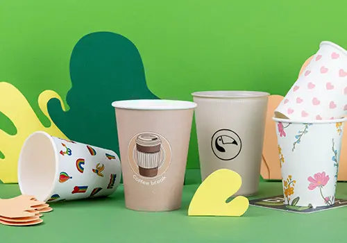 Diverse bekers weergegeven op een lichtblauw oppervlak, met verschillende ontwerpen en labels, waaronder "Alma & Auer" en "Indie Roasters."