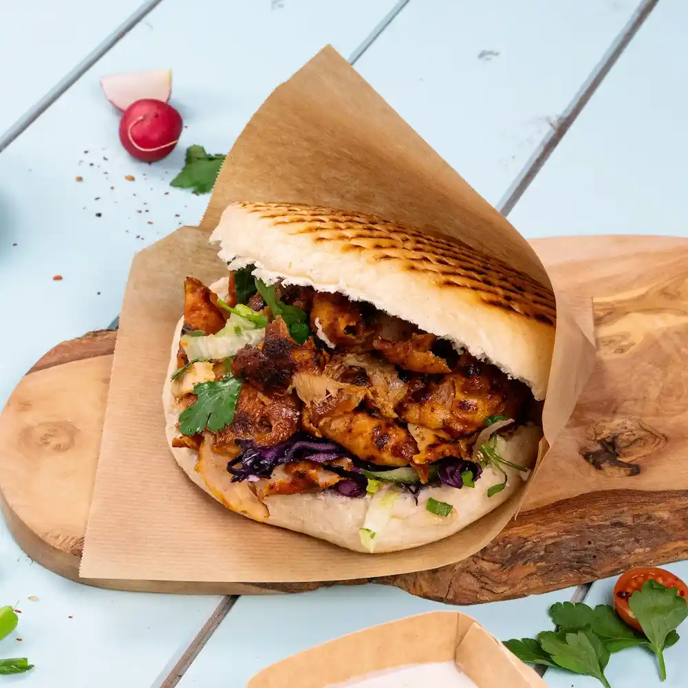 Een gevulde pita sandwich met gegrild kip, sla, paarse kool en koriander op een houten plank.