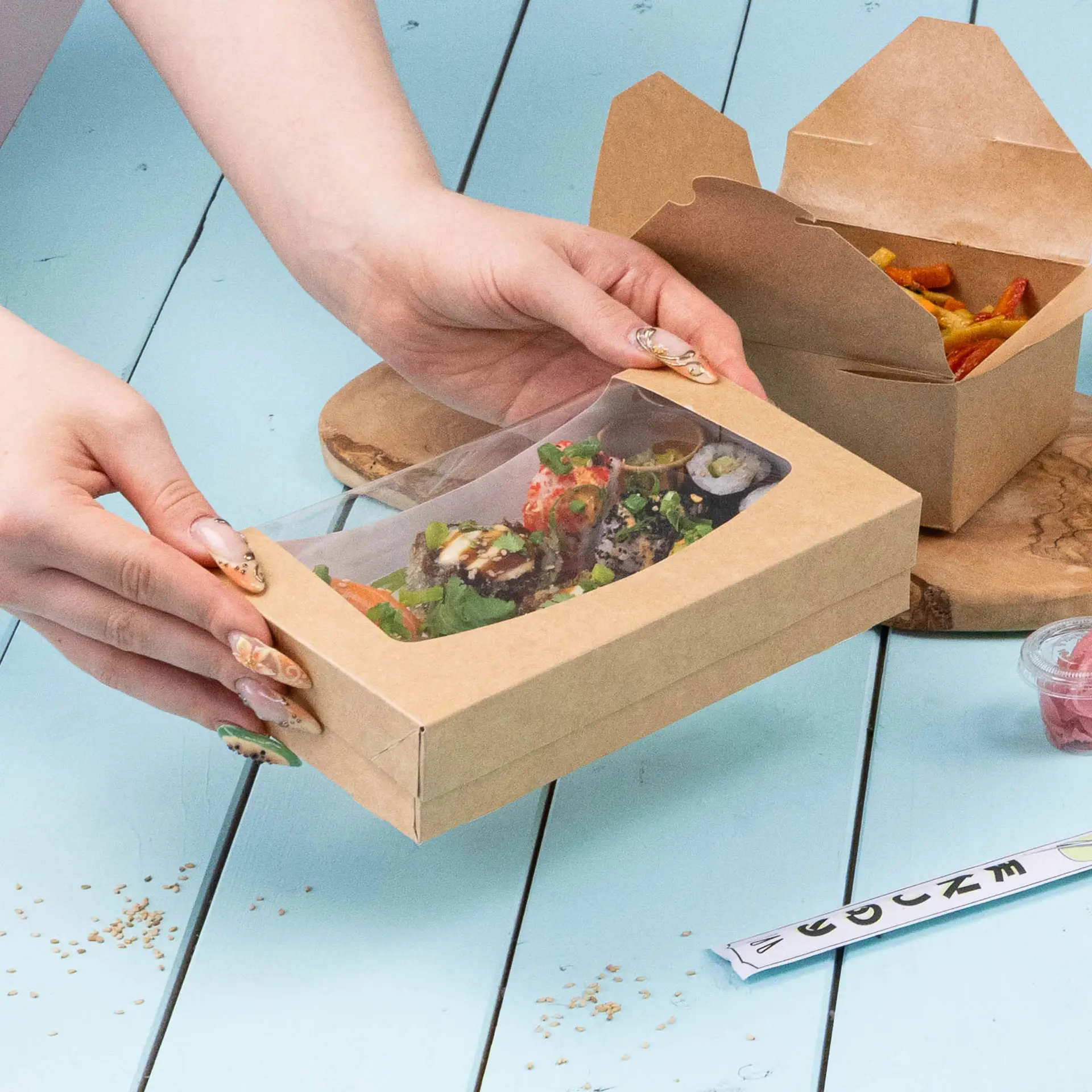Een kartonnen doos met raam met een sandwich met roomkaas, spinazie en fruitspread, geplaatst op een turquoise oppervlak.