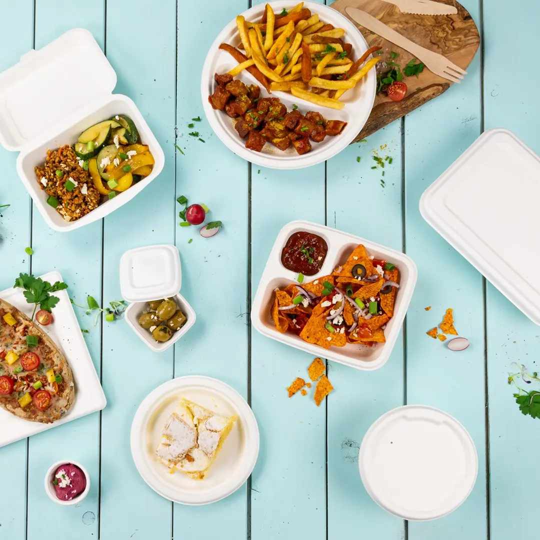 Diverse voedingsmiddelen in afhaalcontainers op een blauwe houten ondergrond, waaronder friet, nacho's en een dessert.