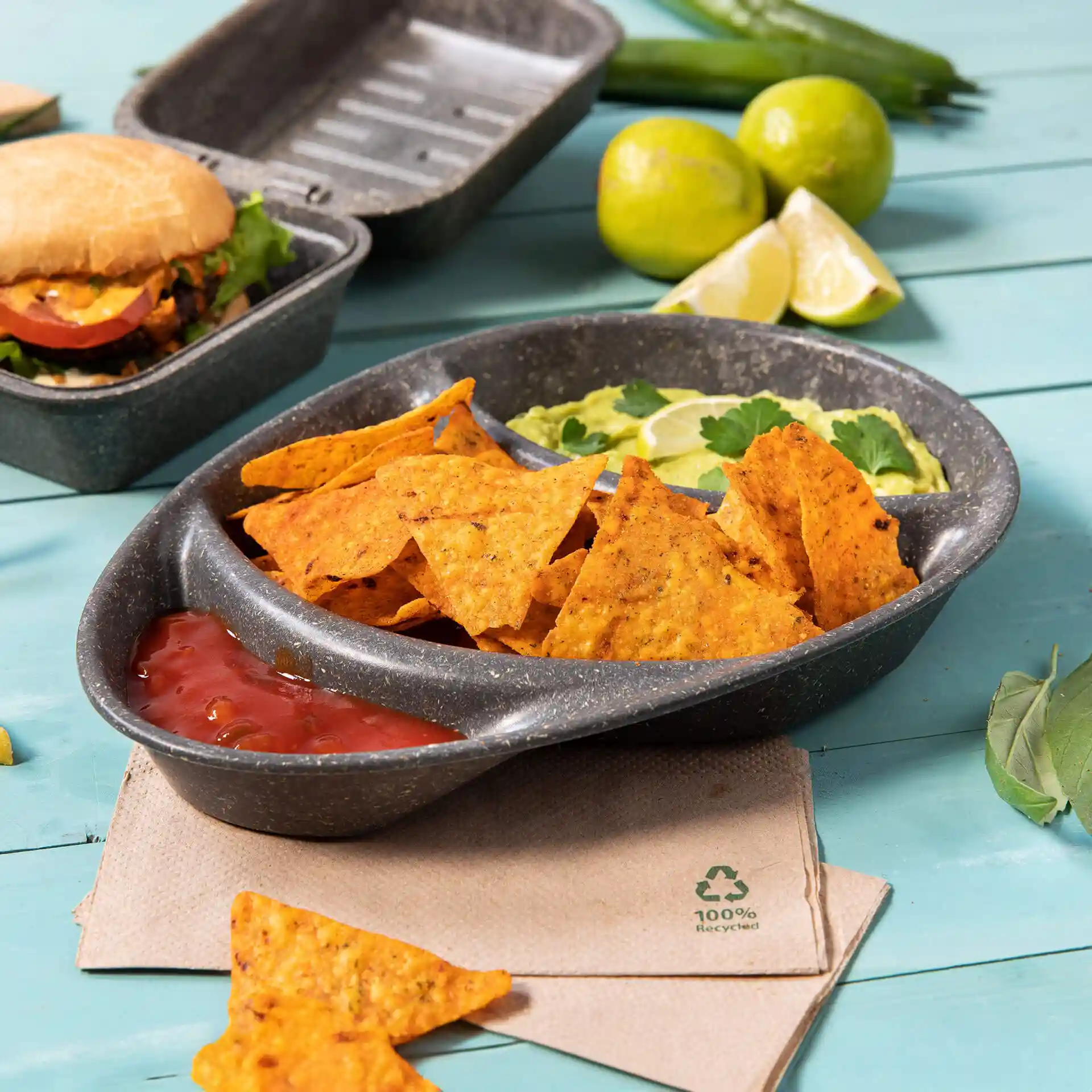 Herbruikbaar verdeeld bord met drie compartimenten, gevuld met nacho's, salsa en guacamole, op een blauwe ondergrond.