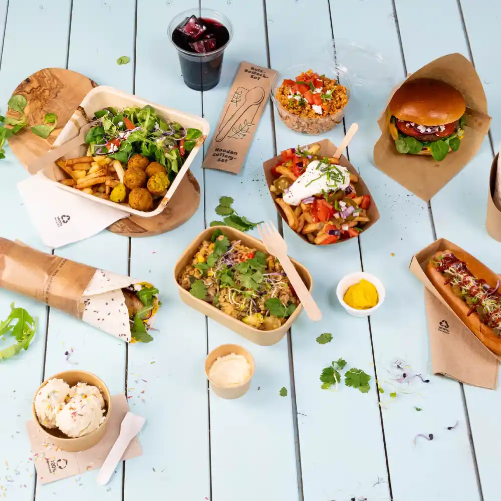 Indeling van verschillende cateringgerechten op een lichtblauwe tafel, inclusief salades, hamburgers, hotdogs en desserts. Ook een drankje is inbegrepen.