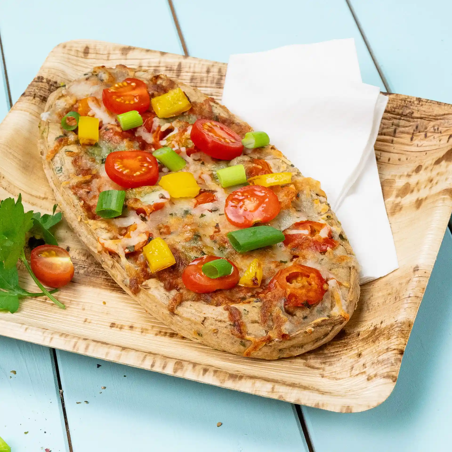 Platbrood belegd met cherrytomaten, gele paprika en lente-uitjes op een houten bord met een servet.
