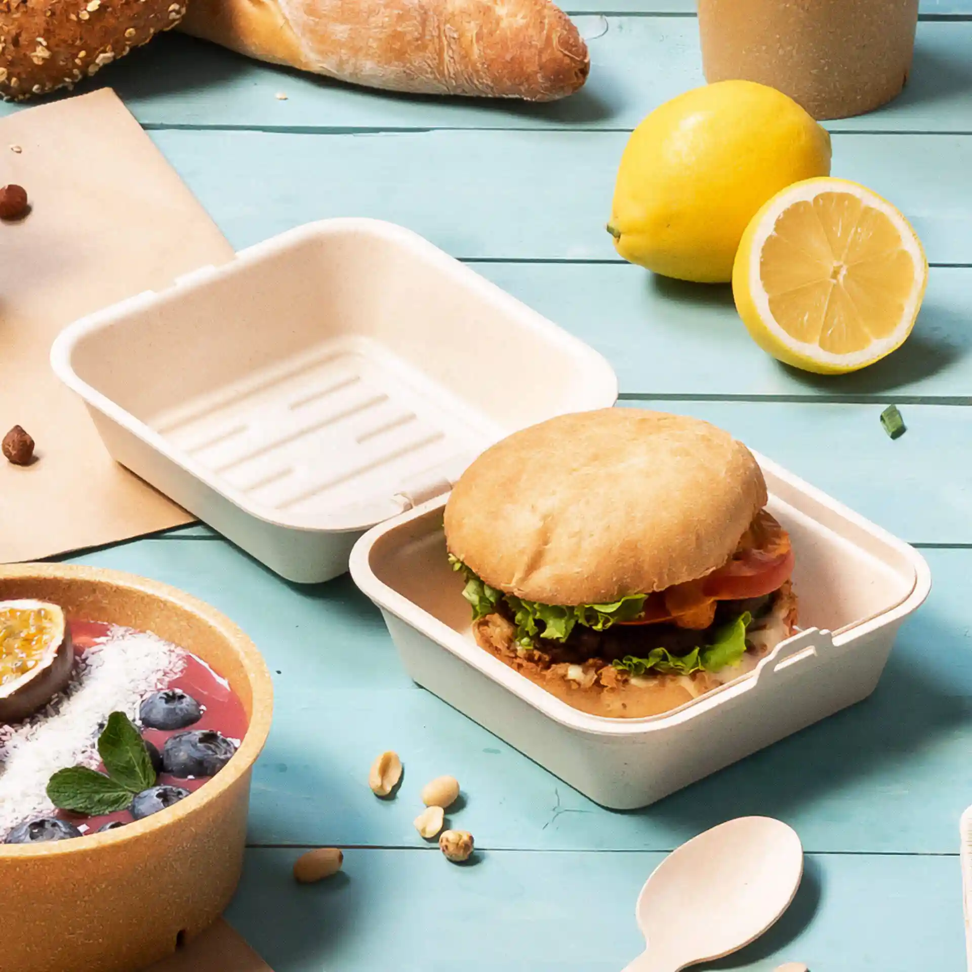 Herbruikbare burgerdoos in crèmewit met een burger erin, omringd door voedsel op een blauwe ondergrond.