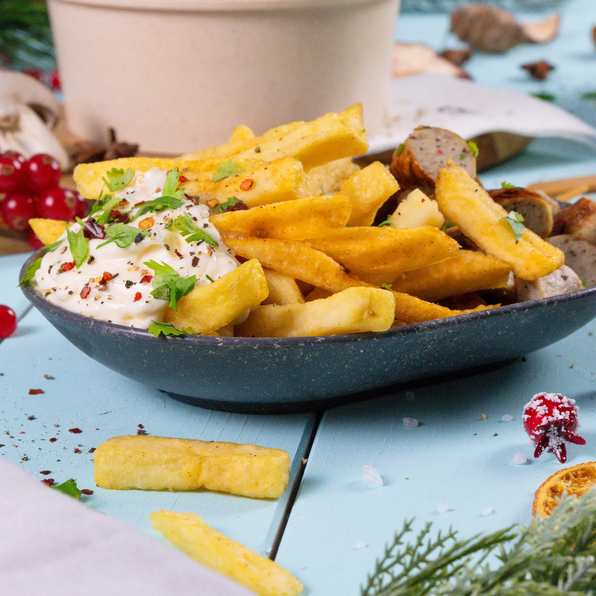 Een ovale herbruikbare snackschaal gevuld met frietjes, getopt met rode pepers en koriander; in de buurt groene en rode paprika's, een vork en snacks.