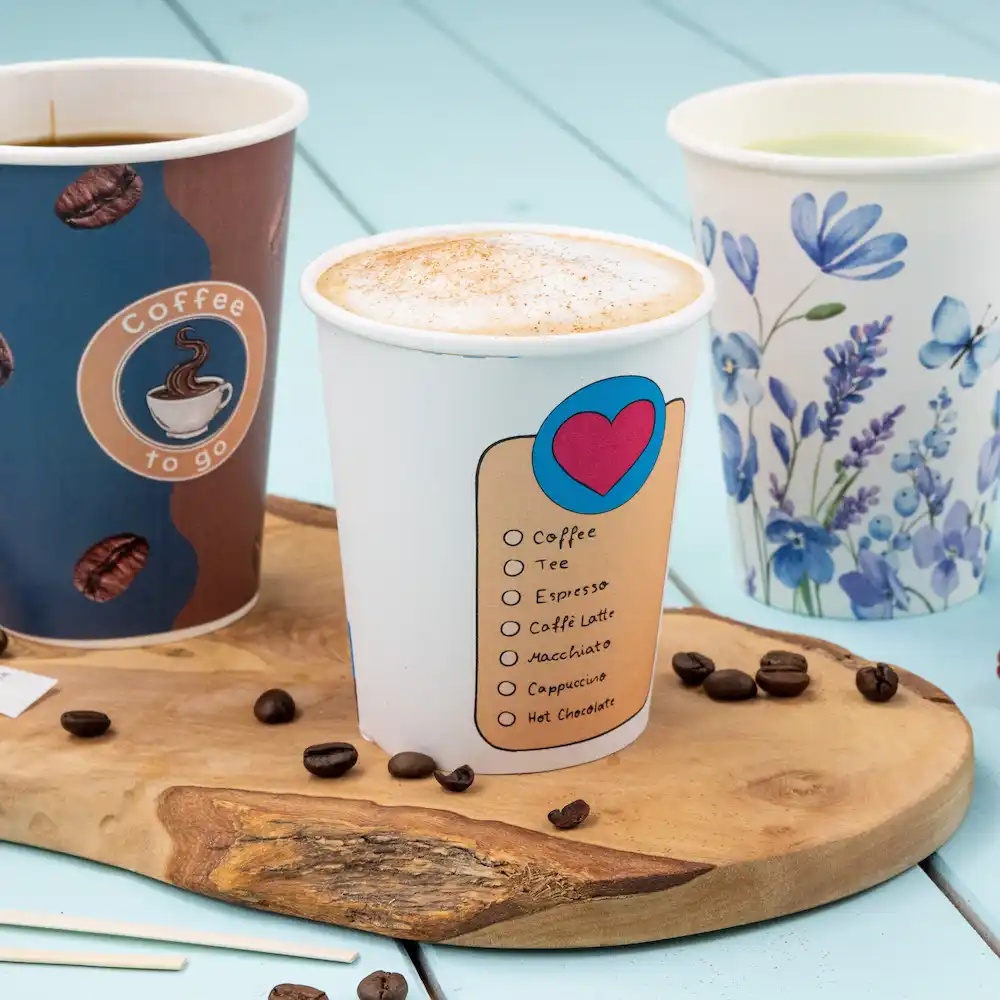 Drie papieren bekers gevuld met dranken, waaronder een koffiekom met een checklist voor drankopties, op een houten oppervlak.
