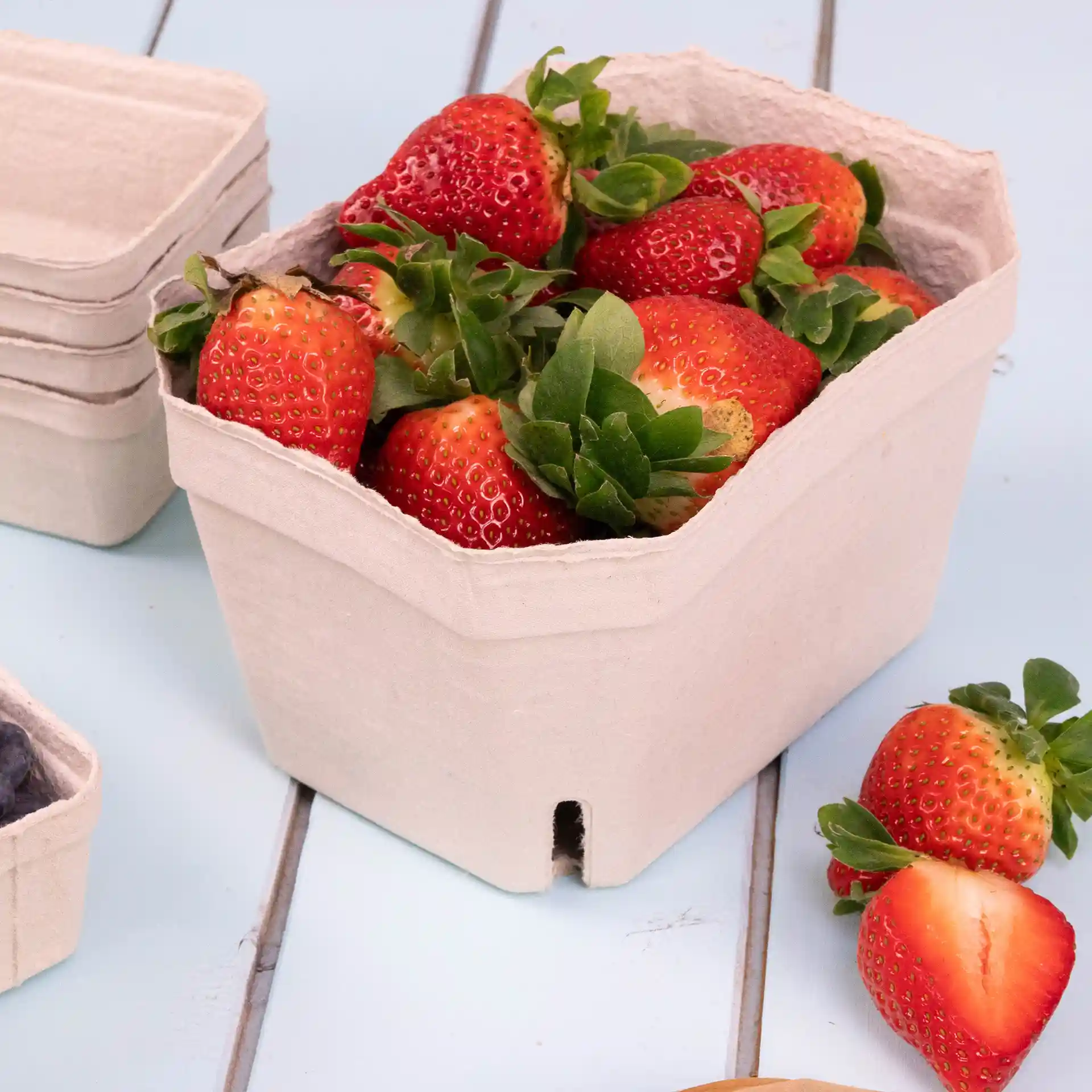 Container van houtpulp met meerdere aardbeien, met extra lege containers op de achtergrond.