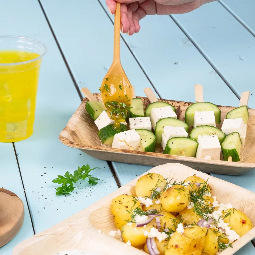 Houten spiesen met komkommer en kaasblokjes, geserveerd met gekruide aardappelen en een drankje.
