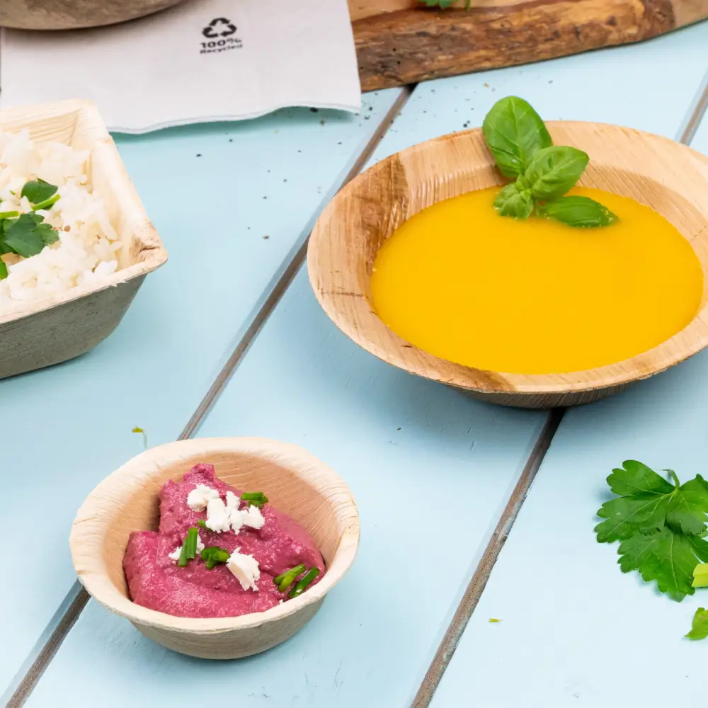 Bamboeschotel gevuld met gele soep, gegarneerd met een basilicumblad; kleinere kom met roze dip, getopt met kruiden; rijst met kruiden in een container in de buurt.