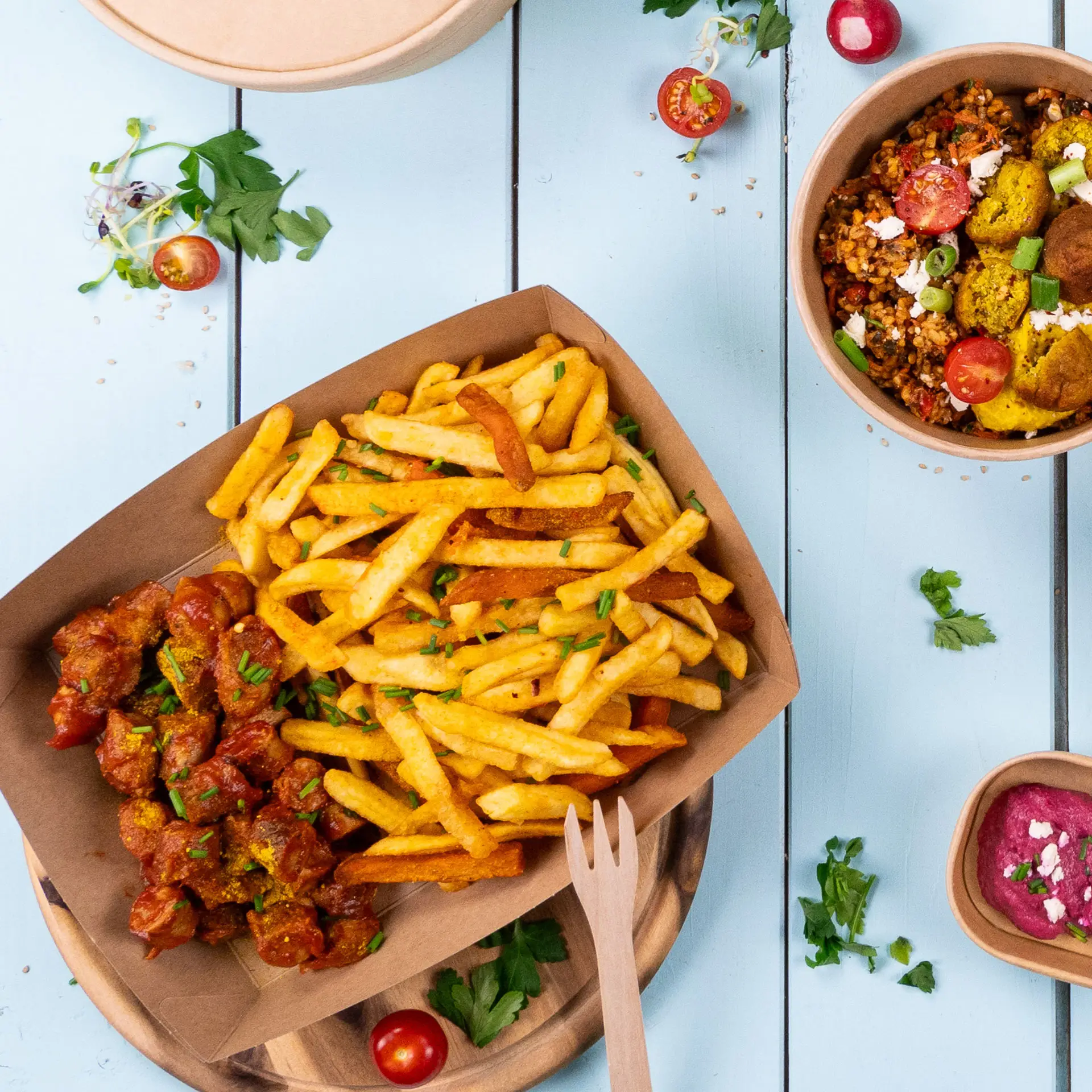 Kartonnen dienblad gevuld met gouden friet en pittige gehaktballetjes, gegarneerd met kruiden, op een blauwe houten ondergrond.