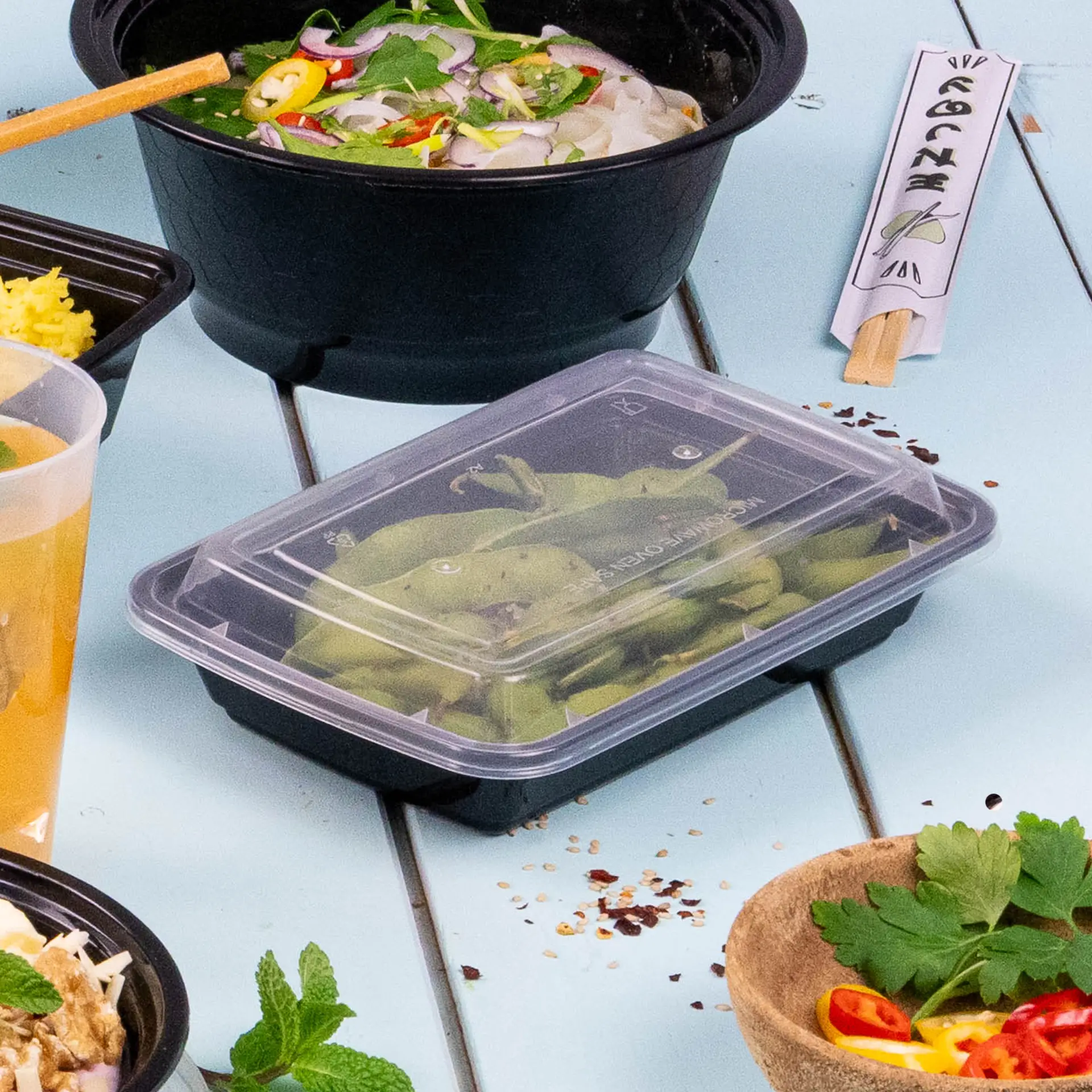 Een rechthoekige zwarte herbruikbare voedselcontainer gevuld met sperziebonen; omringd door andere maaltijdbakken en een drankje.