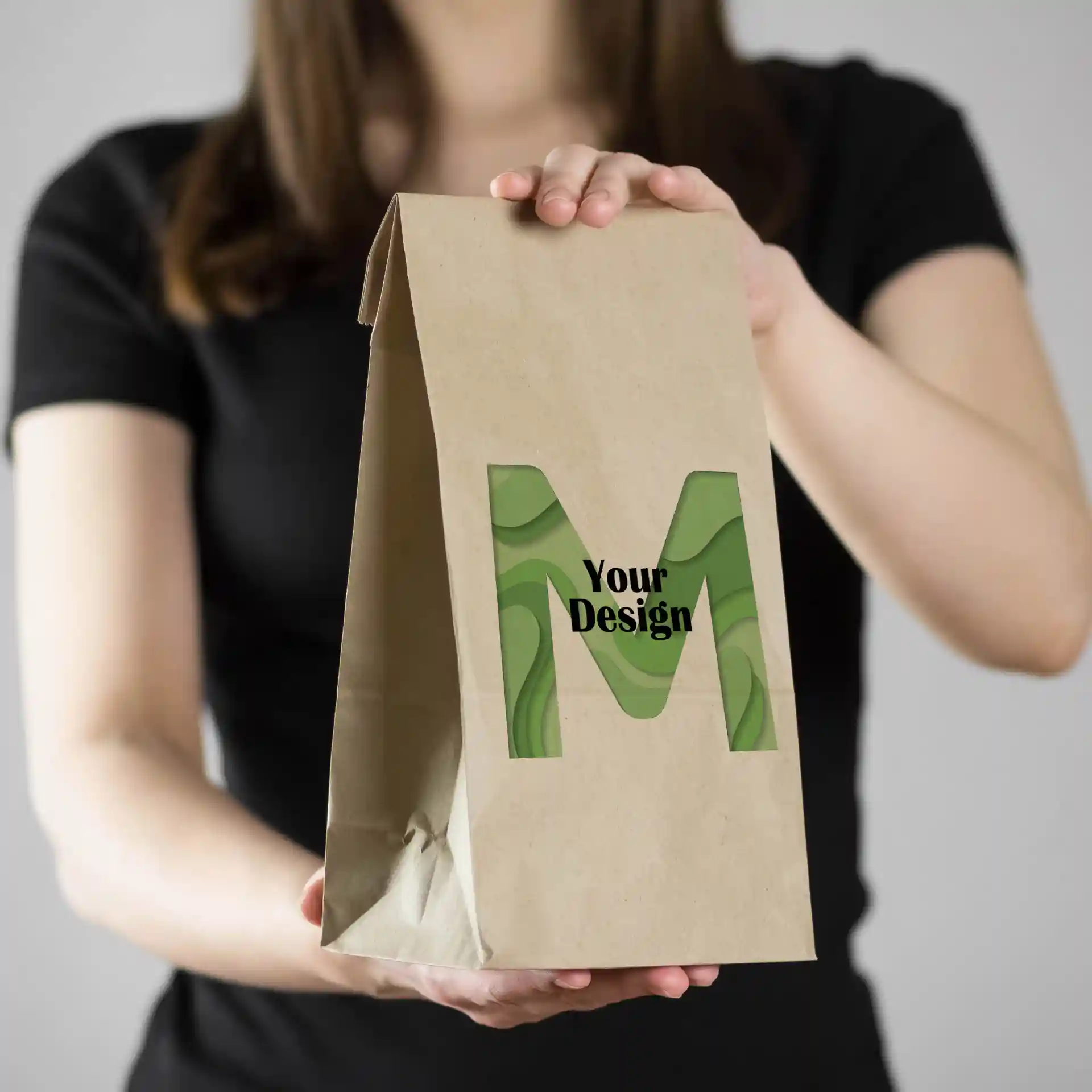 Bruine papieren tas met een groen "M"-ontwerp, vastgehouden door een persoon in een zwart shirt.