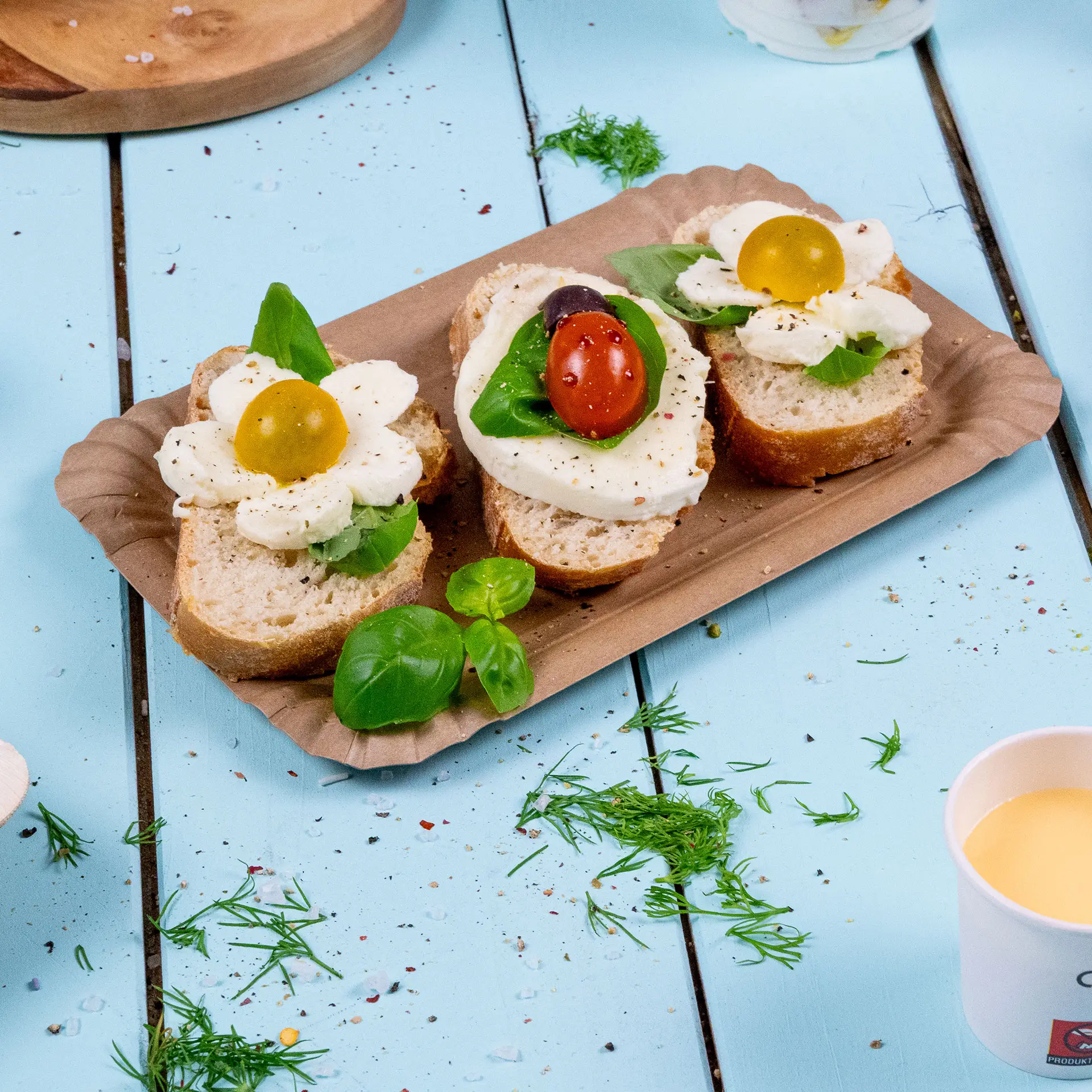 Een rechthoekig bruin kartonnen bord houdt twee open sandwiches met mozzarella, basilicum en cherrytomaten.