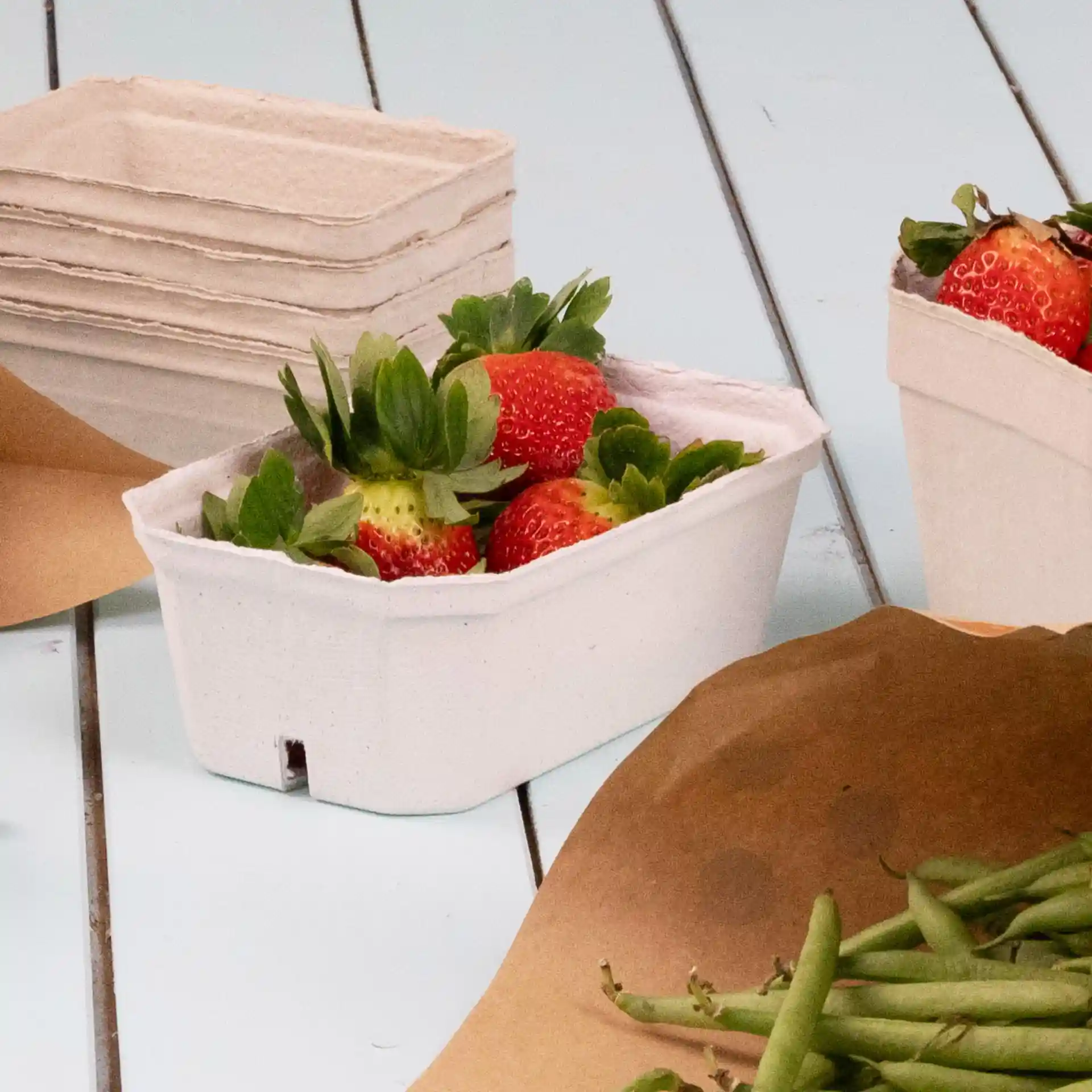 Container met aardbeien, gemaakt van witte houtpulp, met extra lege containers op de achtergrond.