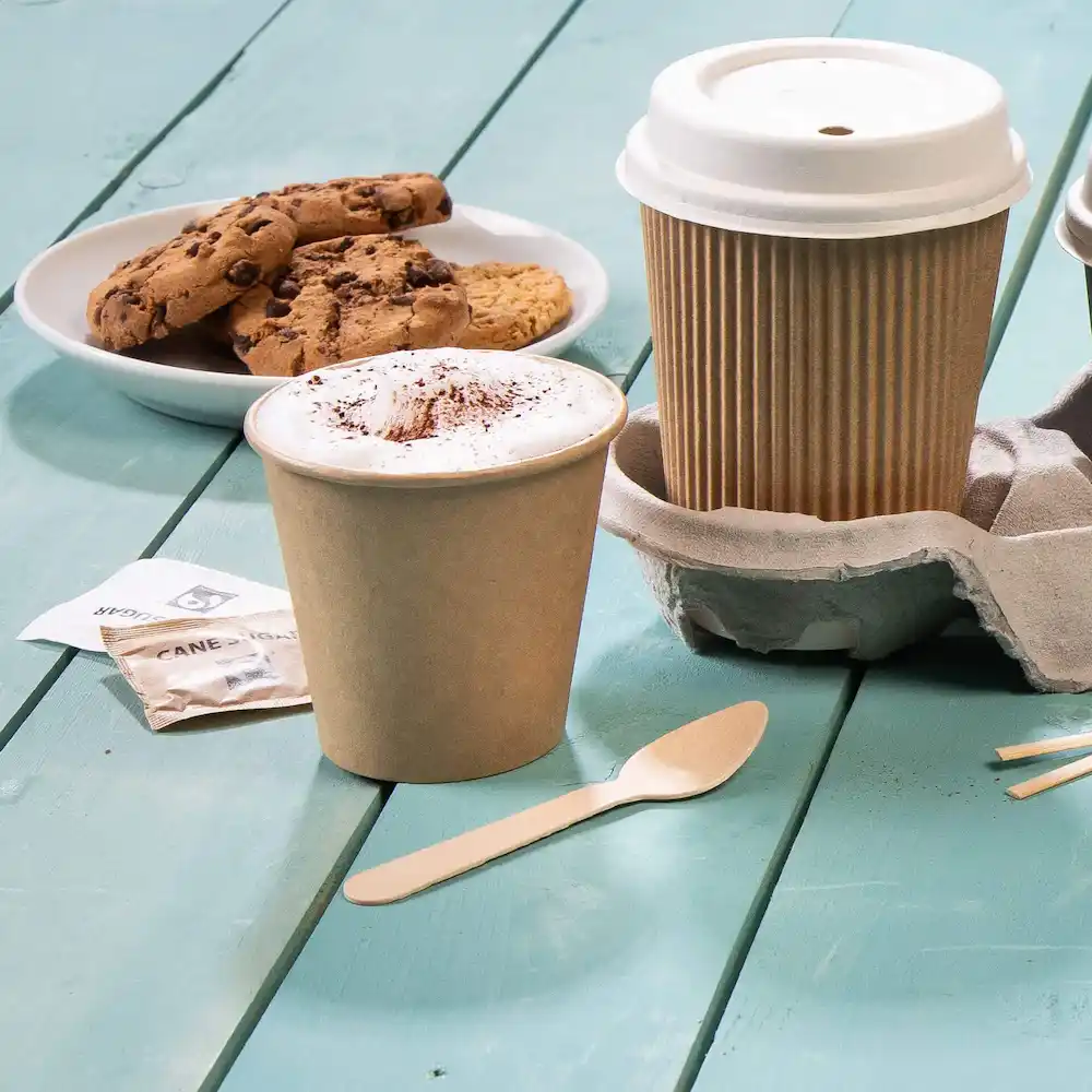 Bruine koffie beker met schuim en cacao, koekjesplateau, houten lepel en bekerhouder op een blauwe houten ondergrond.
