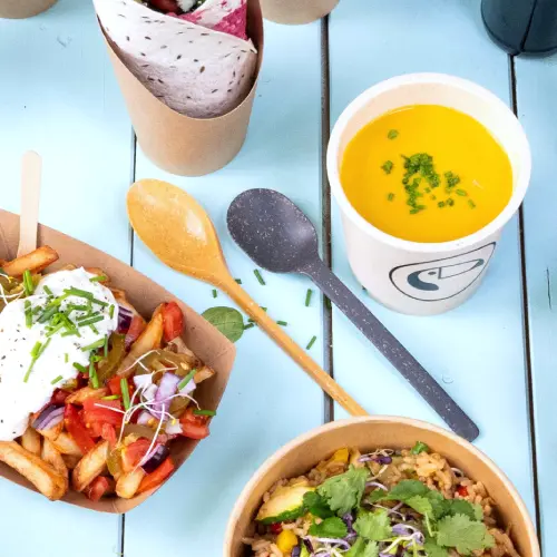 Afbeelding toont verschillende voedingsmiddelen, waaronder frietjes met toppings, een rijstkom met kruiden, een soep in een beker en herbruikbaar bestek op een blauwe ondergrond.