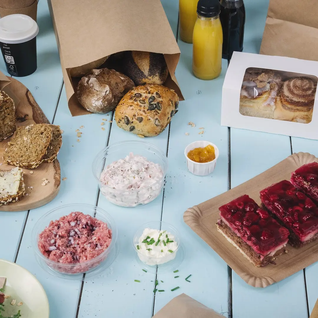 Diverse gebakken goederen, waaronder broodjes, spreads, desserts en dranken op een blauwe houten tafel.
